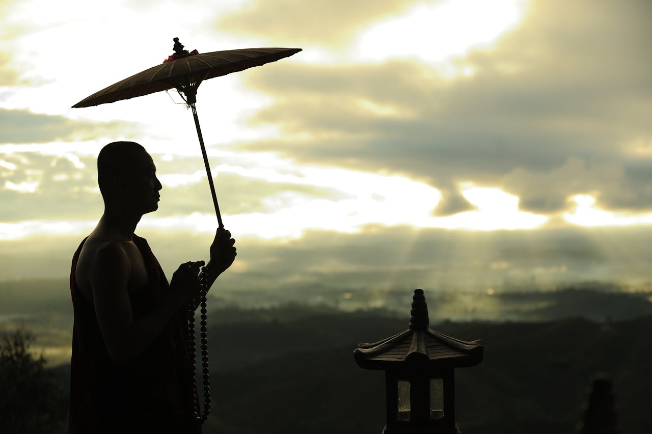 A serene silhouette of a monk standing with a parasol during sunrise, invoking peacefulness.