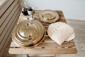 A communion setup with a chalice, wine decanter, flatbread, and golden plates on a wooden table.