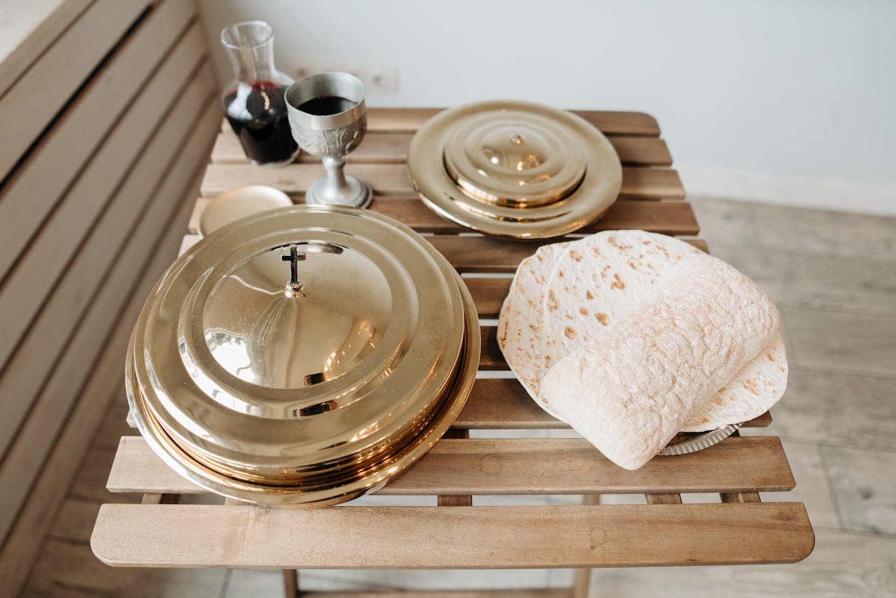 A communion setup with a chalice, wine decanter, flatbread, and golden plates on a wooden table.